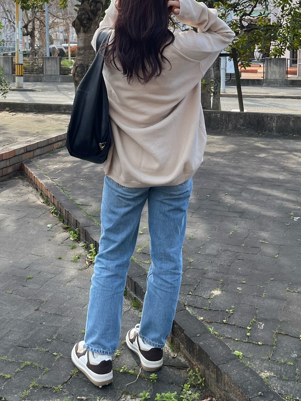 ブラック系のバッグ、ブルー系のデニムパンツ、ブラウン系のスニーカーを着用したレディースの春コーディネートの2枚目の写真