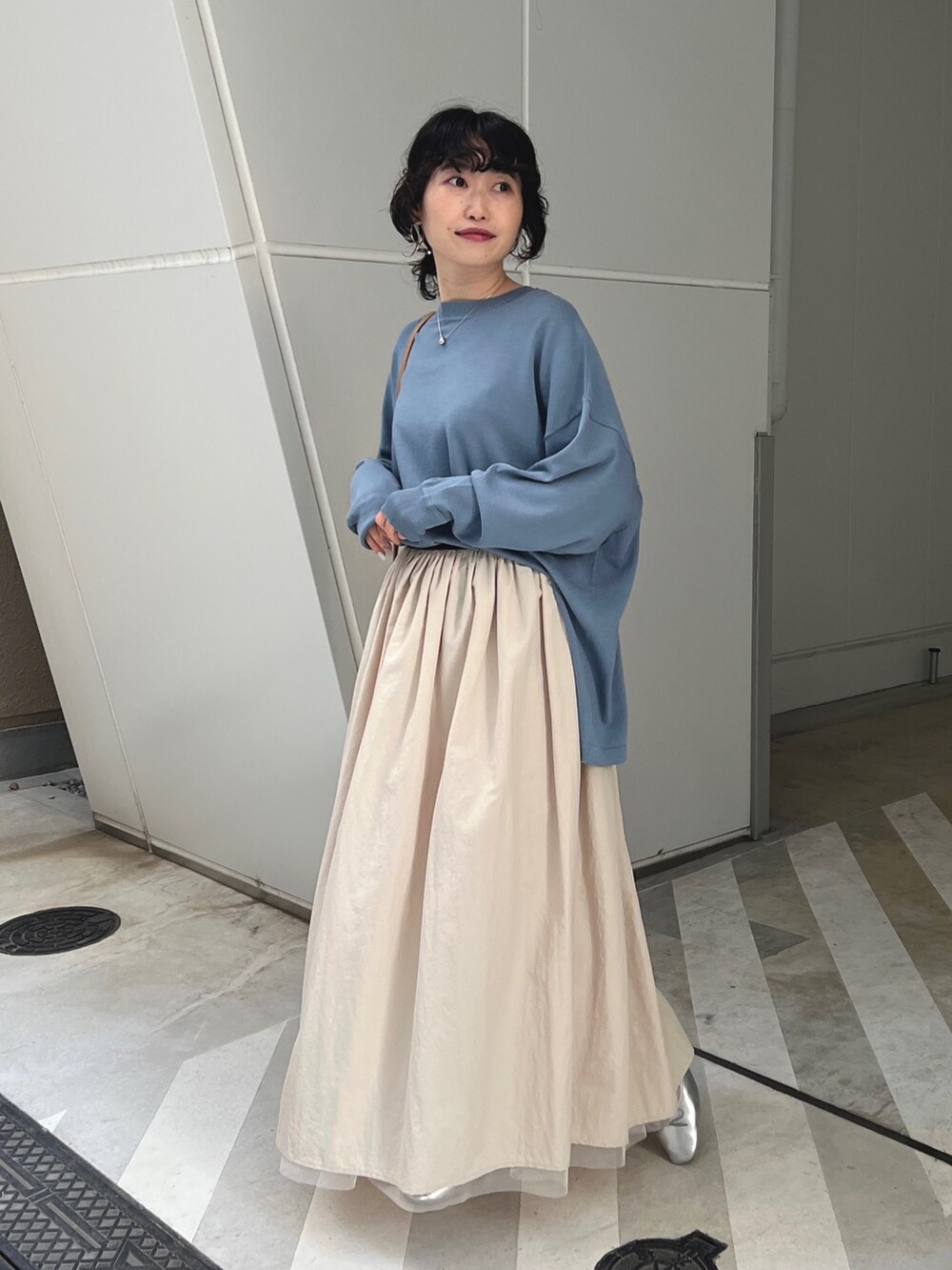 ブルー系のニット/セーター、ホワイト系のスカート、シルバー系のバレエシューズを着用したレディースの春コーディネートの2枚目の写真