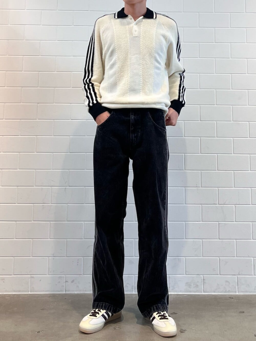 ブラック系のデニムパンツ、ホワイト系のニット/セーター、ホワイト系のスニーカーを着用したメンズの秋コーディネートの2枚目の写真