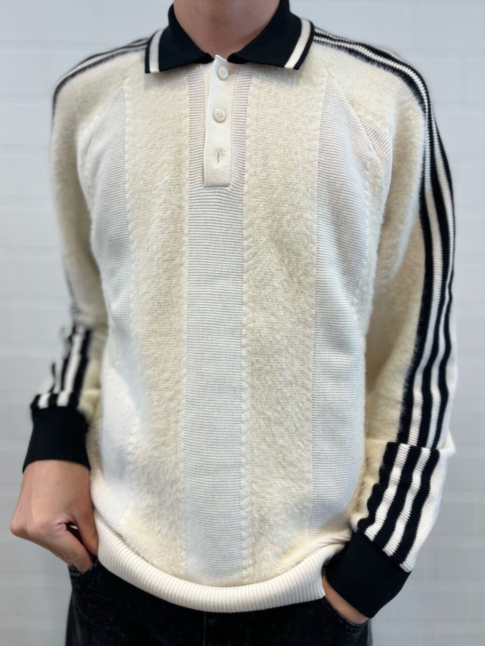 ブラック系のデニムパンツ、ホワイト系のニット/セーター、ホワイト系のスニーカーを着用したメンズの秋コーディネートの4枚目の写真