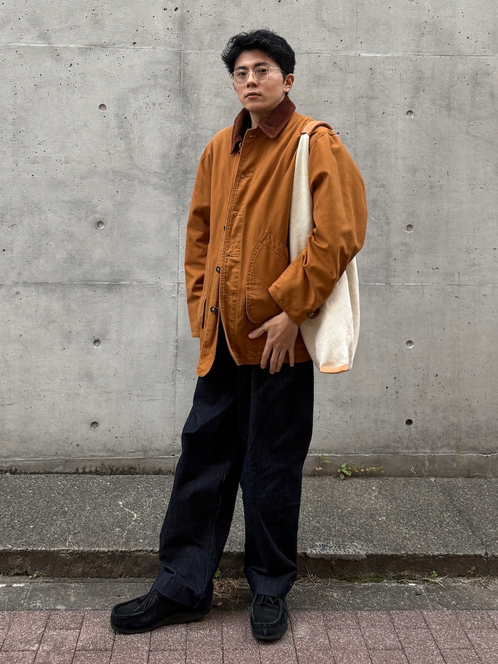 オレンジ系のジャケット/アウター、ベージュ系のトートバッグ、ブルー系のデニムパンツを着用したメンズの秋コーディネートの2枚目の写真