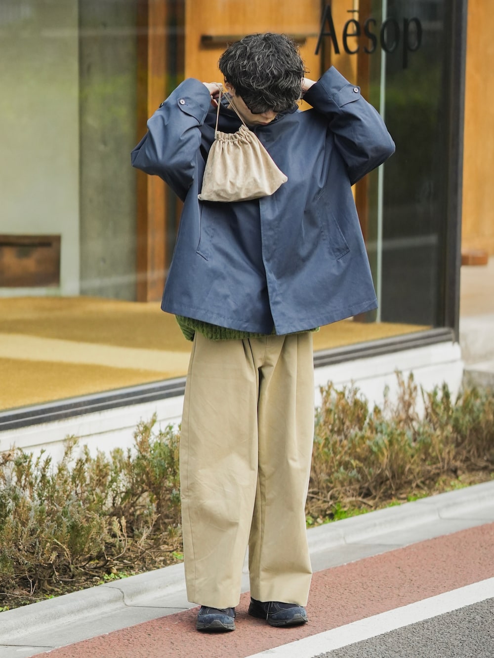 ブルー系のステンカラーコート、ベージュ系のショルダーバッグ、ベージュ系のチノパンツを着用したメンズの秋コーディネートの3枚目の写真