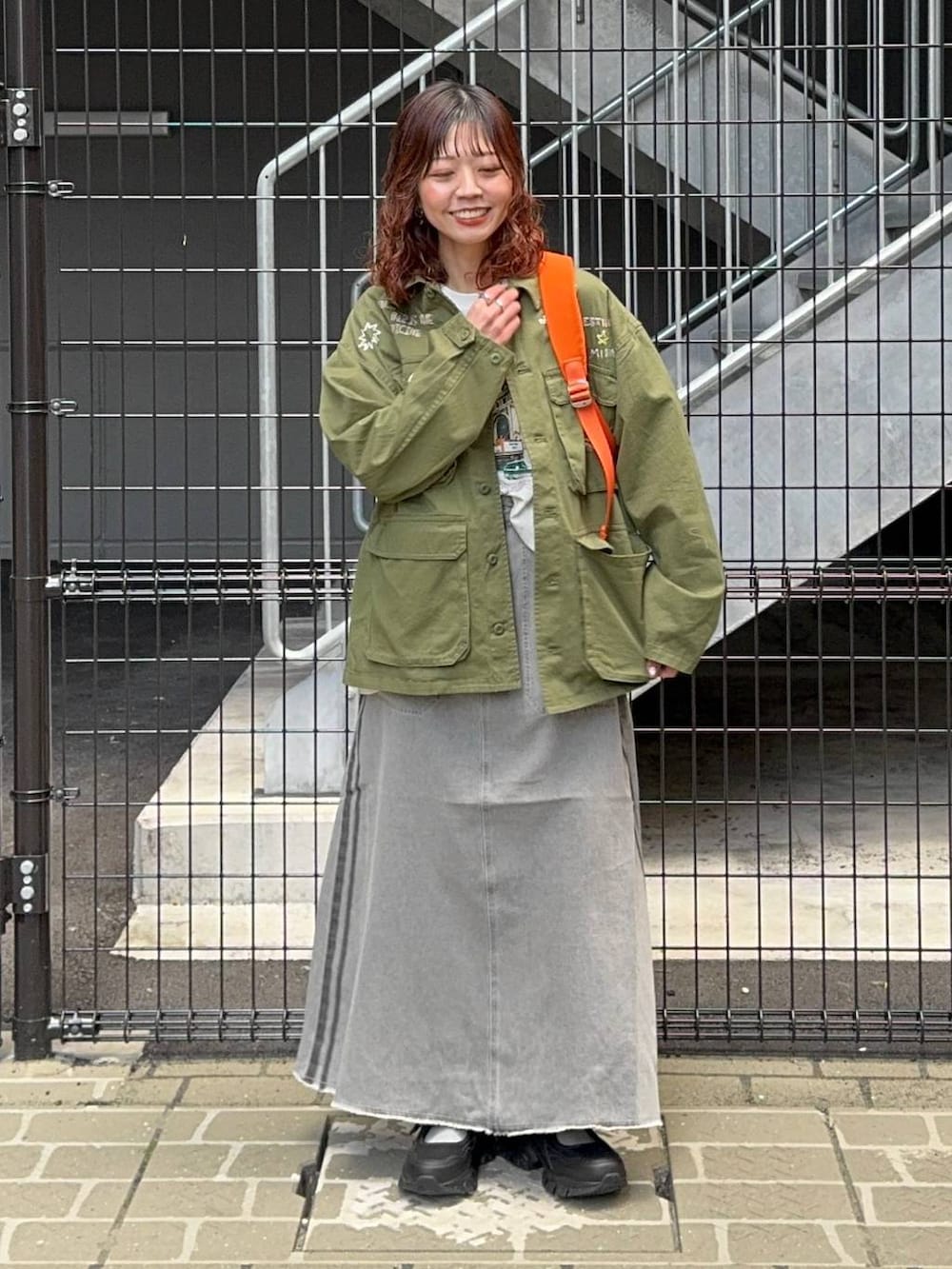 グリーン系のシャツ/ブラウス、オレンジ系のバックパック/リュック、ホワイト系のTシャツ/カットソーを着用したレディースの春コーディネートの2枚目の写真