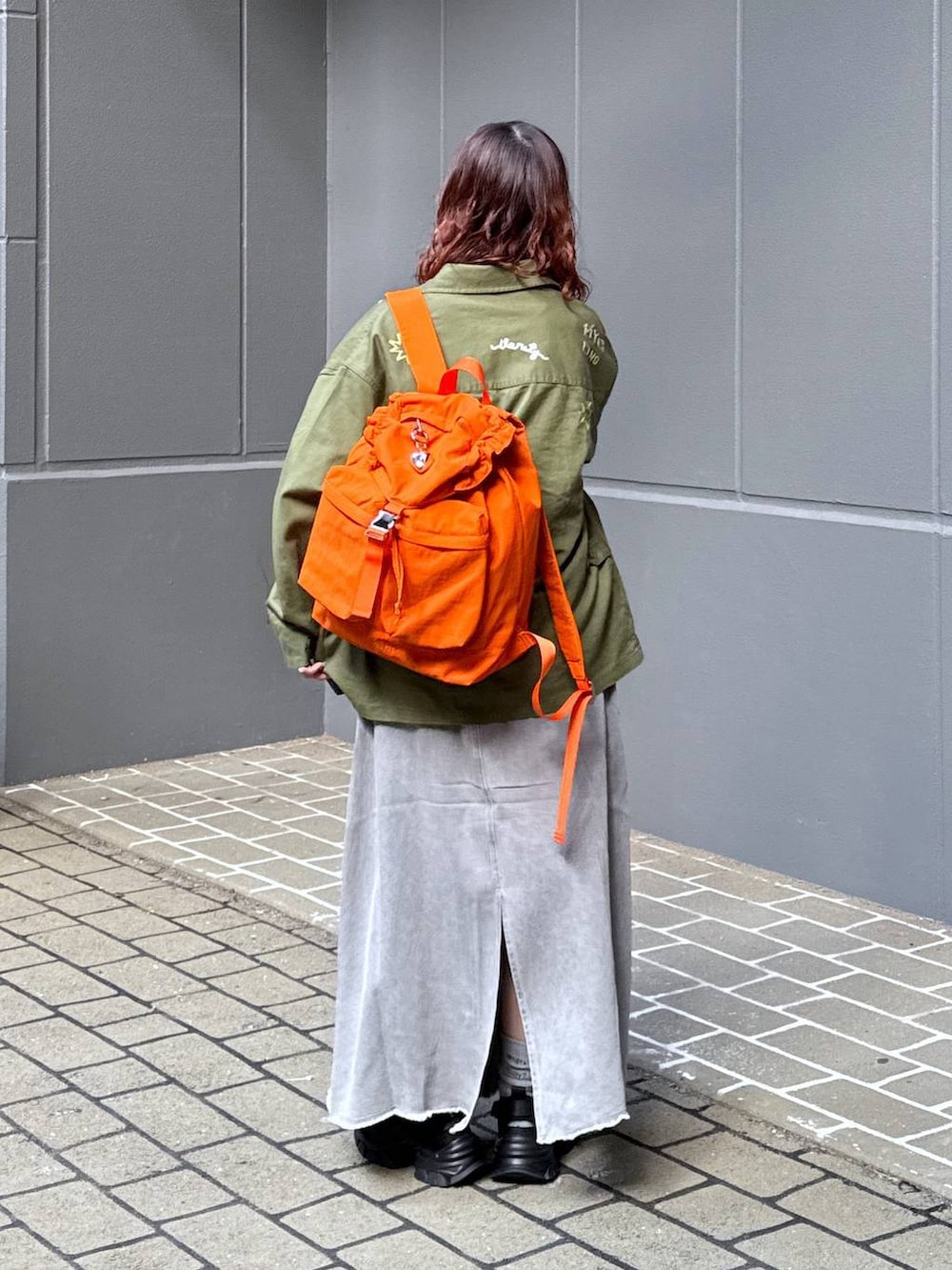 グリーン系のシャツ/ブラウス、オレンジ系のバックパック/リュック、ホワイト系のTシャツ/カットソーを着用したレディースの春コーディネートの4枚目の写真