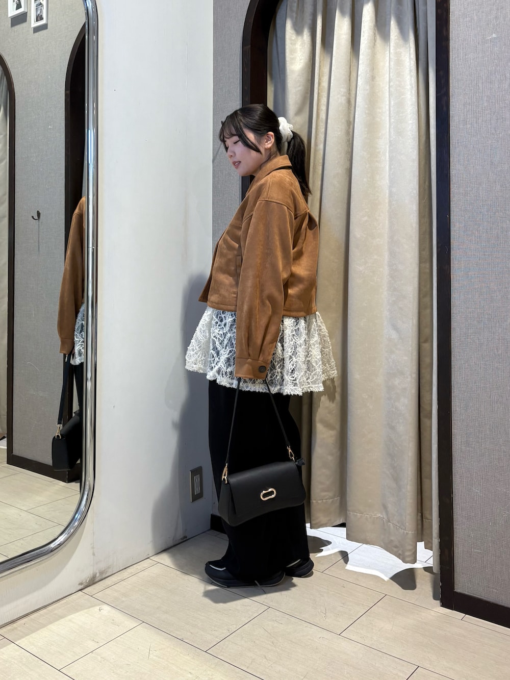 イエロー系のブルゾン、ブラック系のショルダーバッグ、ホワイト系のチュニックを着用したレディースの冬コーディネートの2枚目の写真