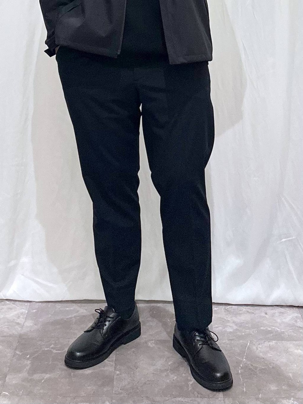 ブルー系のスラックス、ブラック系のニット/セーター、ブラック系のショルダーバッグを着用したメンズの春コーディネートの3枚目の写真