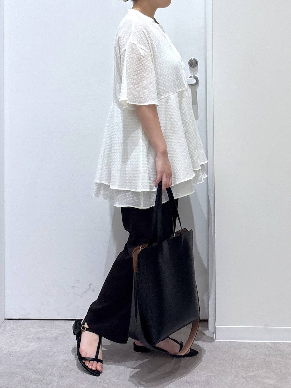 ブラック系のトートバッグ、ブラウン系のスラックス、ブラック系のサンダルを着用したレディースの夏コーディネートの2枚目の写真