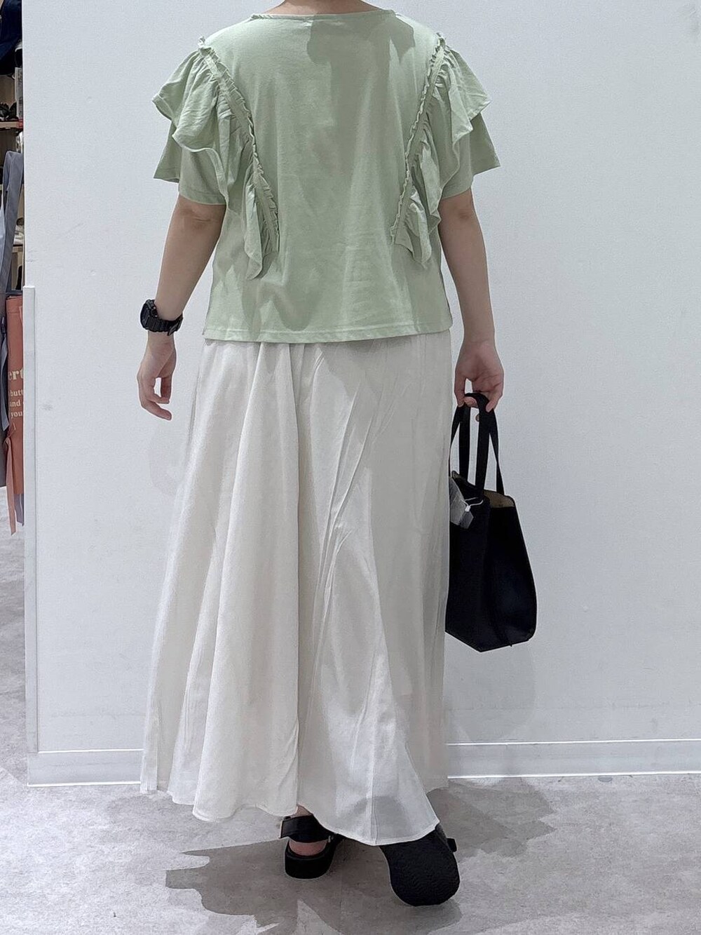 ブラック系のショルダーバッグ、ホワイト系のスカート、グリーン系のTシャツ/カットソーを着用したレディースの夏コーディネートの3枚目の写真