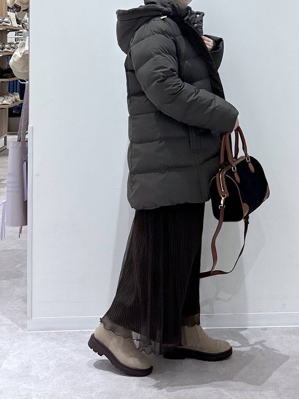 ブラウン系のダウンジャケット/コート、ベージュ系のブーツ、ブラック系のボストンバッグを着用したレディースの冬コーディネートの2枚目の写真