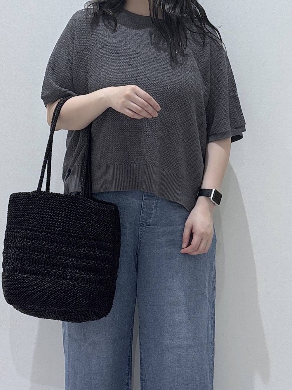ブルー系のデニムパンツ、ブラック系のクラッチバッグ、グレー系のニット/セーターを着用したレディースの春コーディネートの2枚目の写真