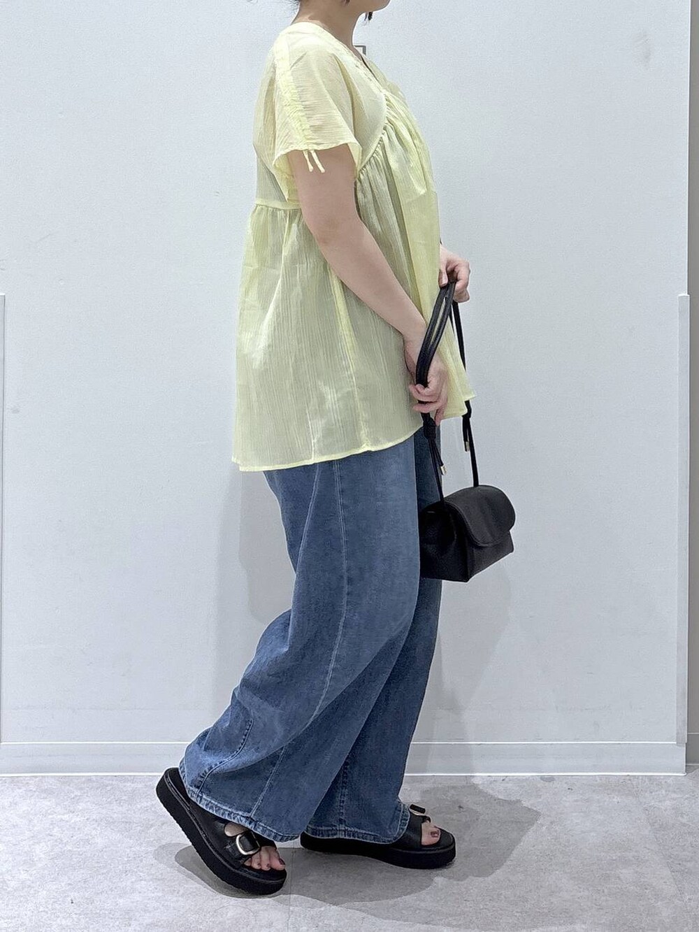 ブラック系のショルダーバッグ、ブルー系のデニムパンツ、イエロー系のシャツ/ブラウスを着用したレディースの夏コーディネートの2枚目の写真