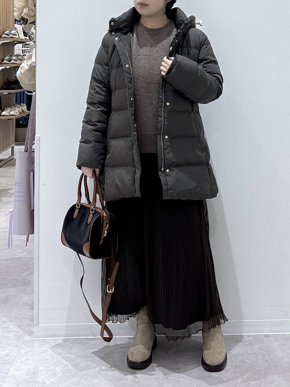 ブラウン系のダウンジャケット/コート、ベージュ系のブーツ、ブラック系のボストンバッグを着用したレディースの冬コーディネートの4枚目の写真