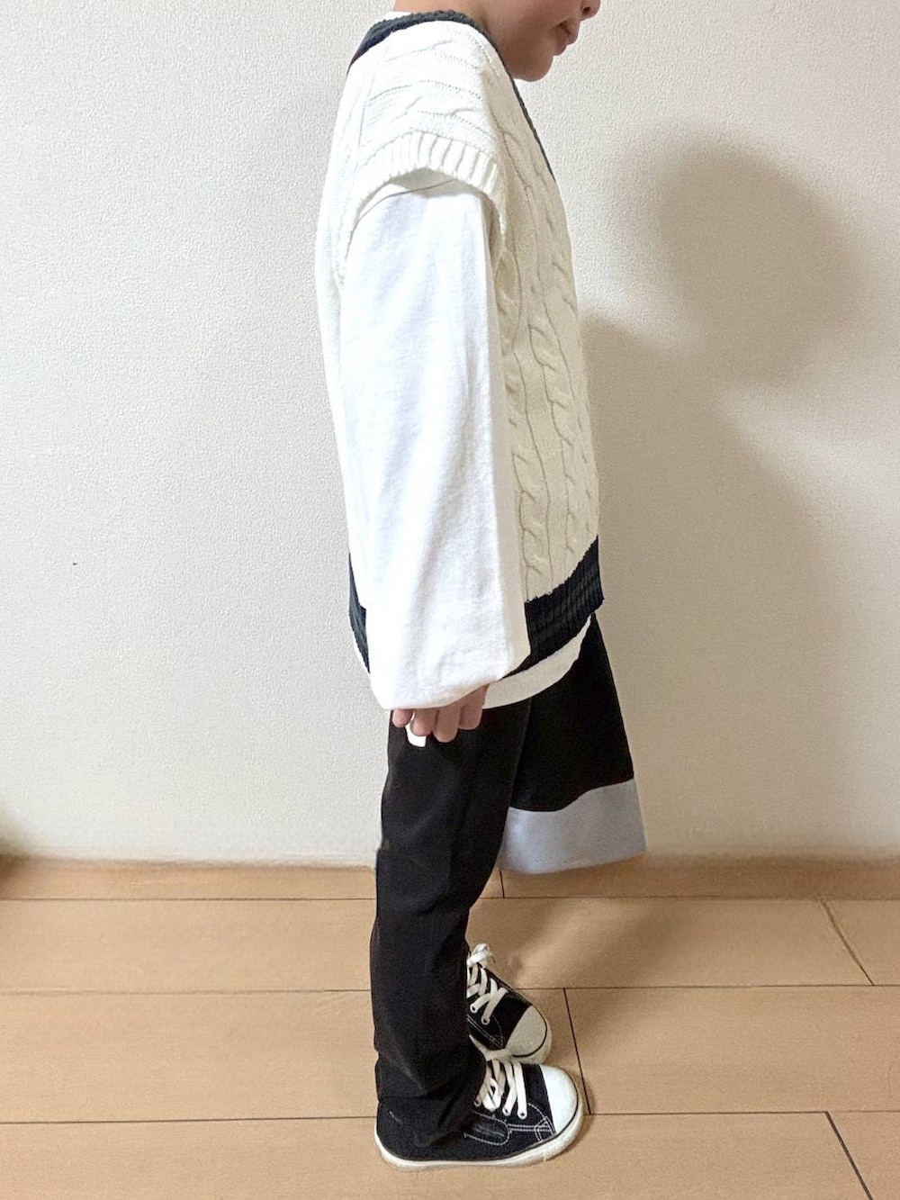 ブラック系のデニムパンツ、ベージュ系のベスト、ブラック系のハンドバッグを着用したキッズの冬コーディネートの2枚目の写真