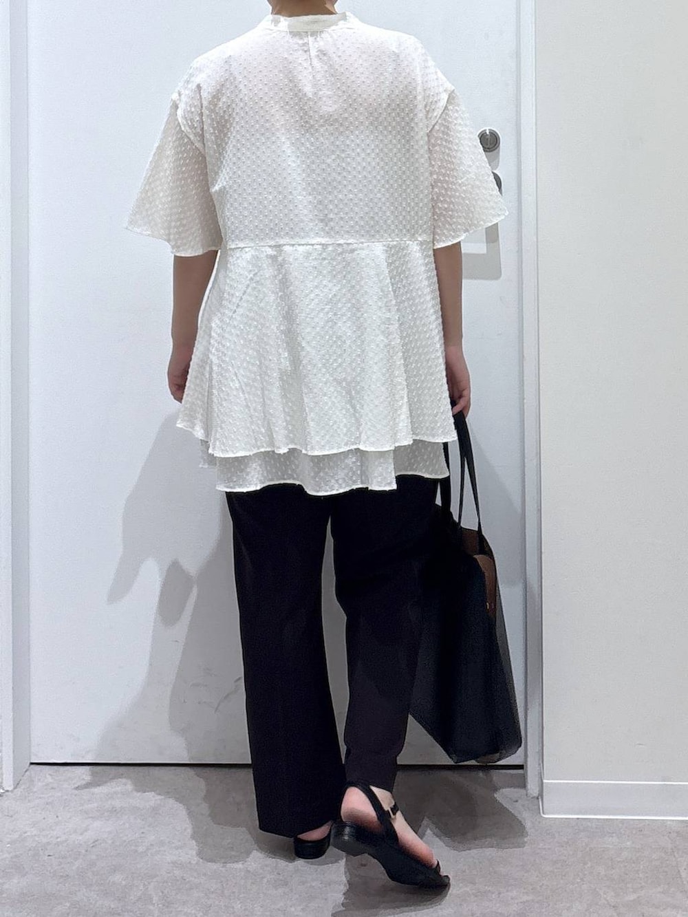 ブラック系のトートバッグ、ブラウン系のスラックス、ブラック系のサンダルを着用したレディースの夏コーディネートの3枚目の写真