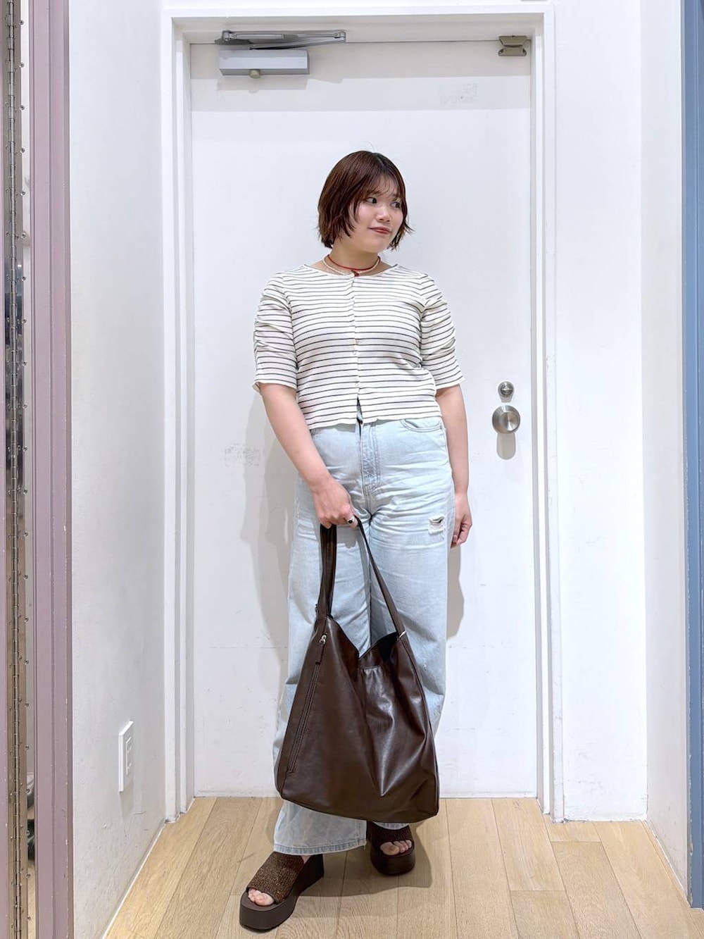 ブルー系のデニムパンツ、ブラウン系のショルダーバッグ、ブラウン系のサンダルを着用したレディースの春コーディネートの2枚目の写真