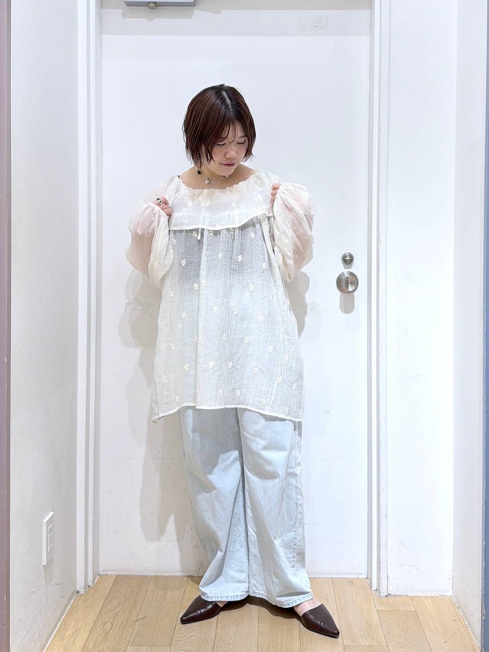 ブルー系のデニムパンツ、ブラウン系のサンダル、ホワイト系のワンピースを着用したレディースの春コーディネートの2枚目の写真