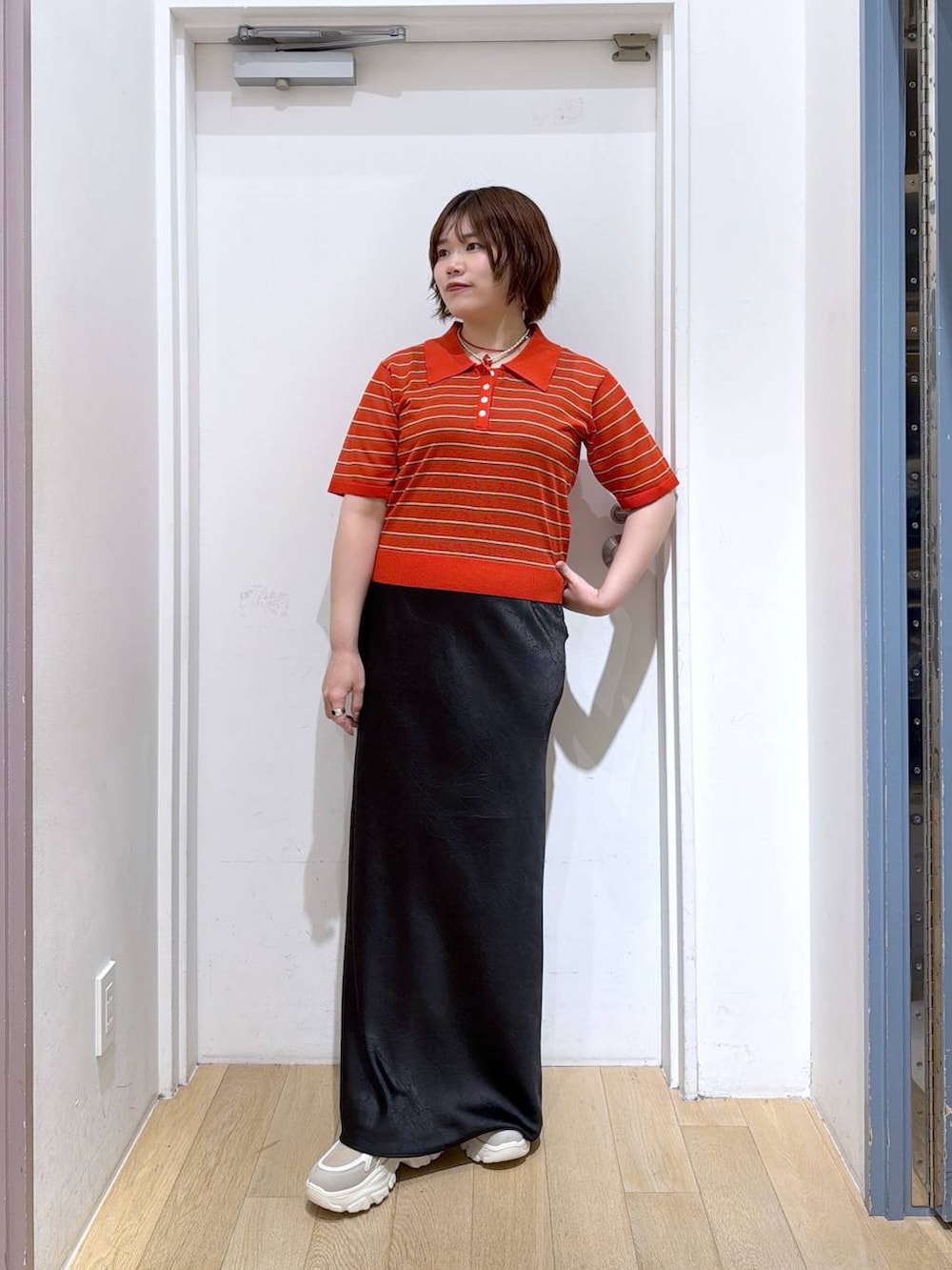 ブラック系のスカート、レッド系のポロシャツ、ベージュ系のスニーカーを着用したレディースの春コーディネートの2枚目の写真