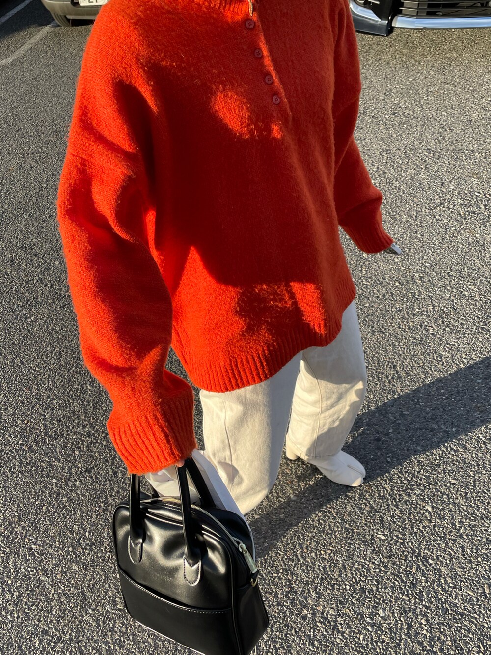 オレンジ系のニット/セーター、ホワイト系のデニムパンツ、ホワイト系のブーツを着用したレディースの秋コーディネートの2枚目の写真