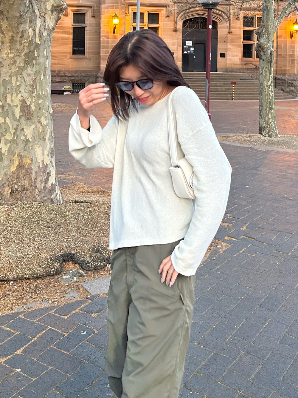 グリーン系のパンツ、ホワイト系のショルダーバッグ、ブラック系のブーツを着用したレディースの秋コーディネートの2枚目の写真