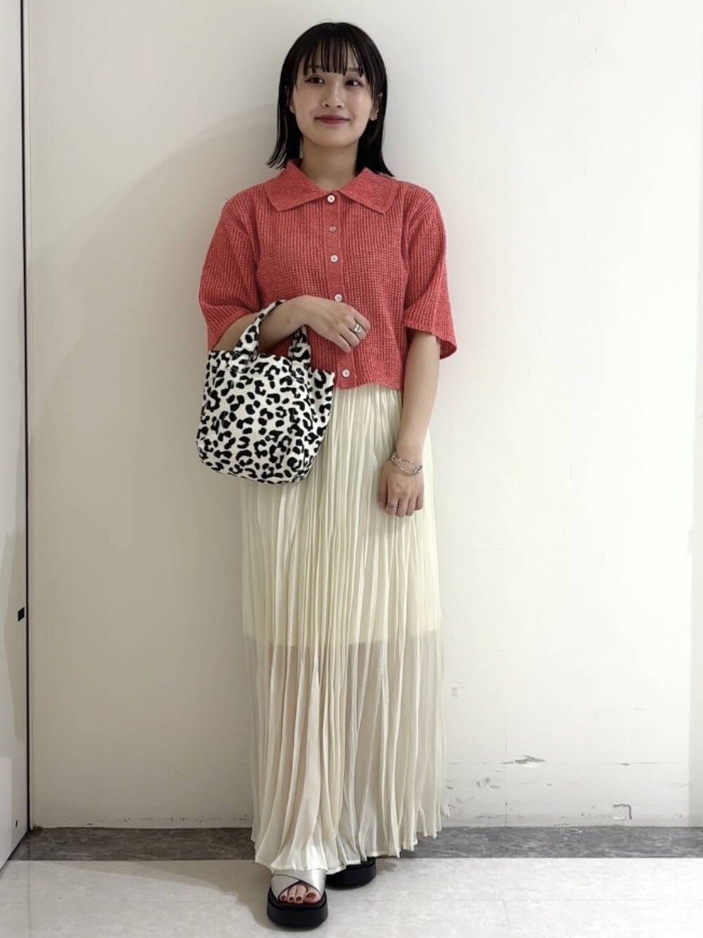 オレンジ系のニット/セーター、シルバー系のサンダル、ホワイト系のスカートを着用したレディースの夏コーディネートの2枚目の写真