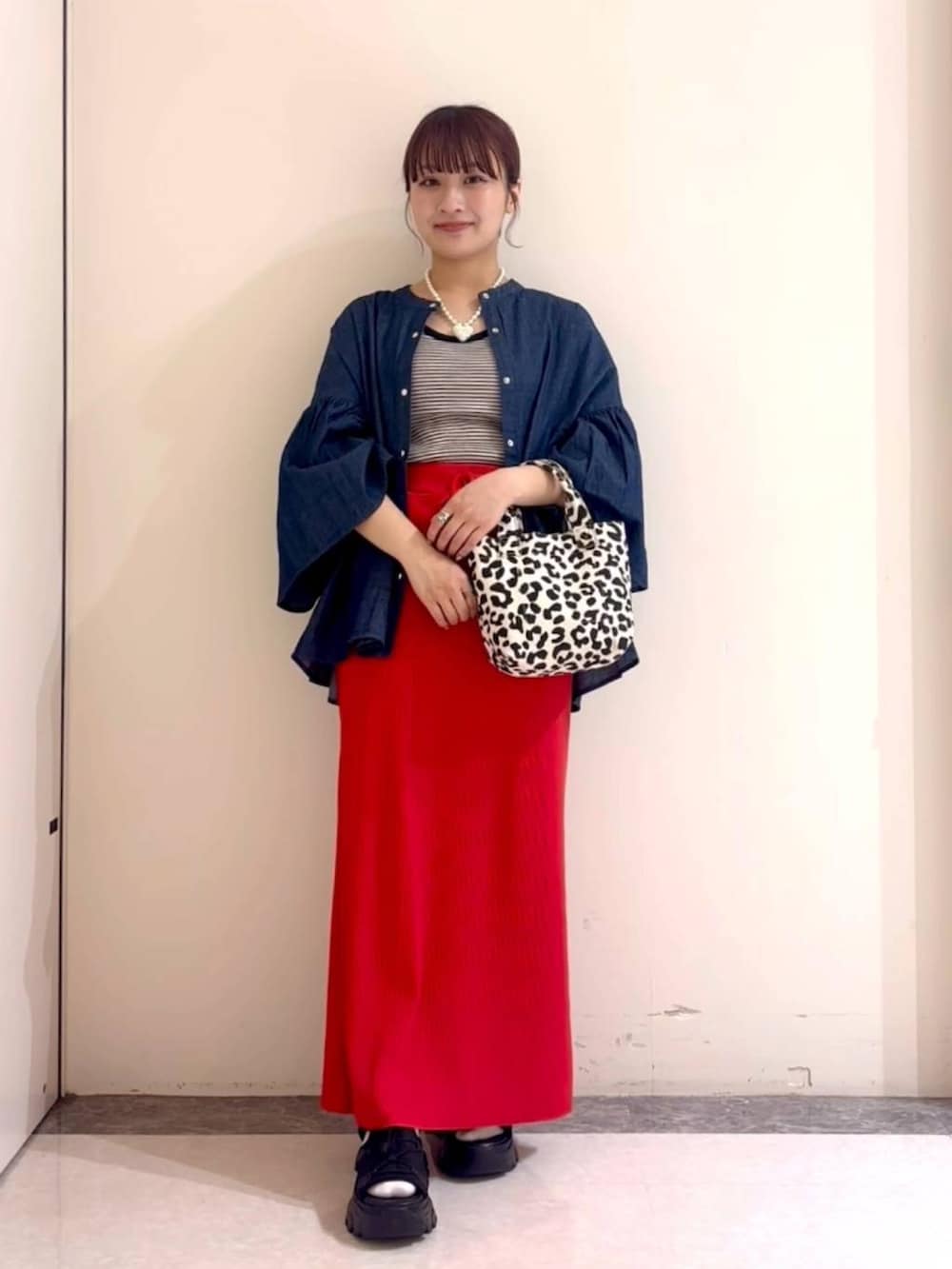 レッド系のスカート、ブラック系のタンクトップ、ブラック系のトートバッグを着用したレディースの春コーディネートの2枚目の写真