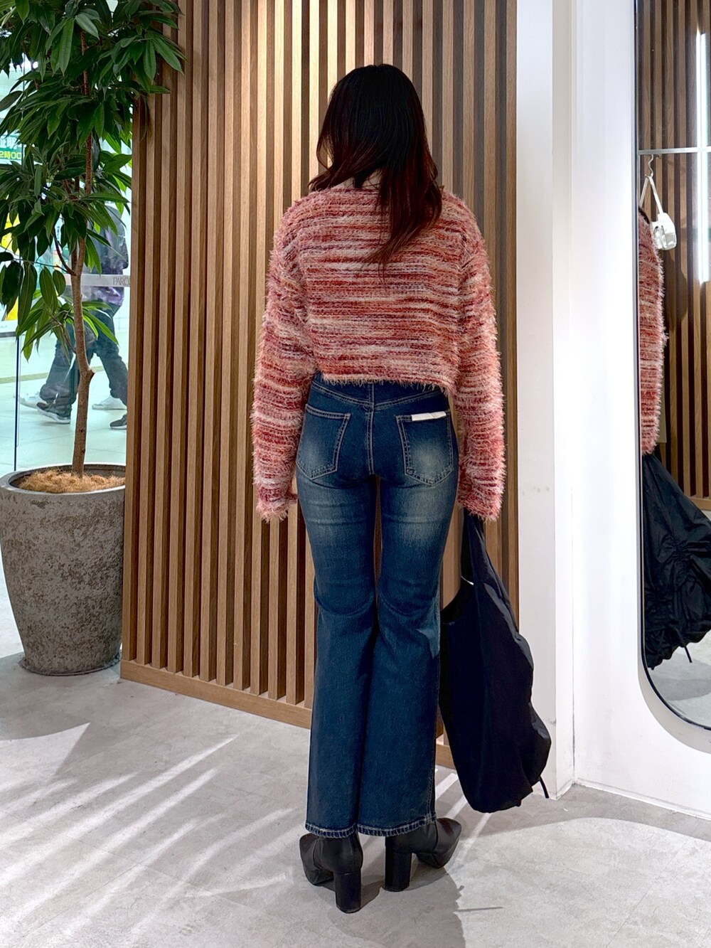 レッド系のニット/セーター、ブルー系のデニムパンツ、ブラック系のトートバッグを着用したレディースの冬コーディネートの2枚目の写真