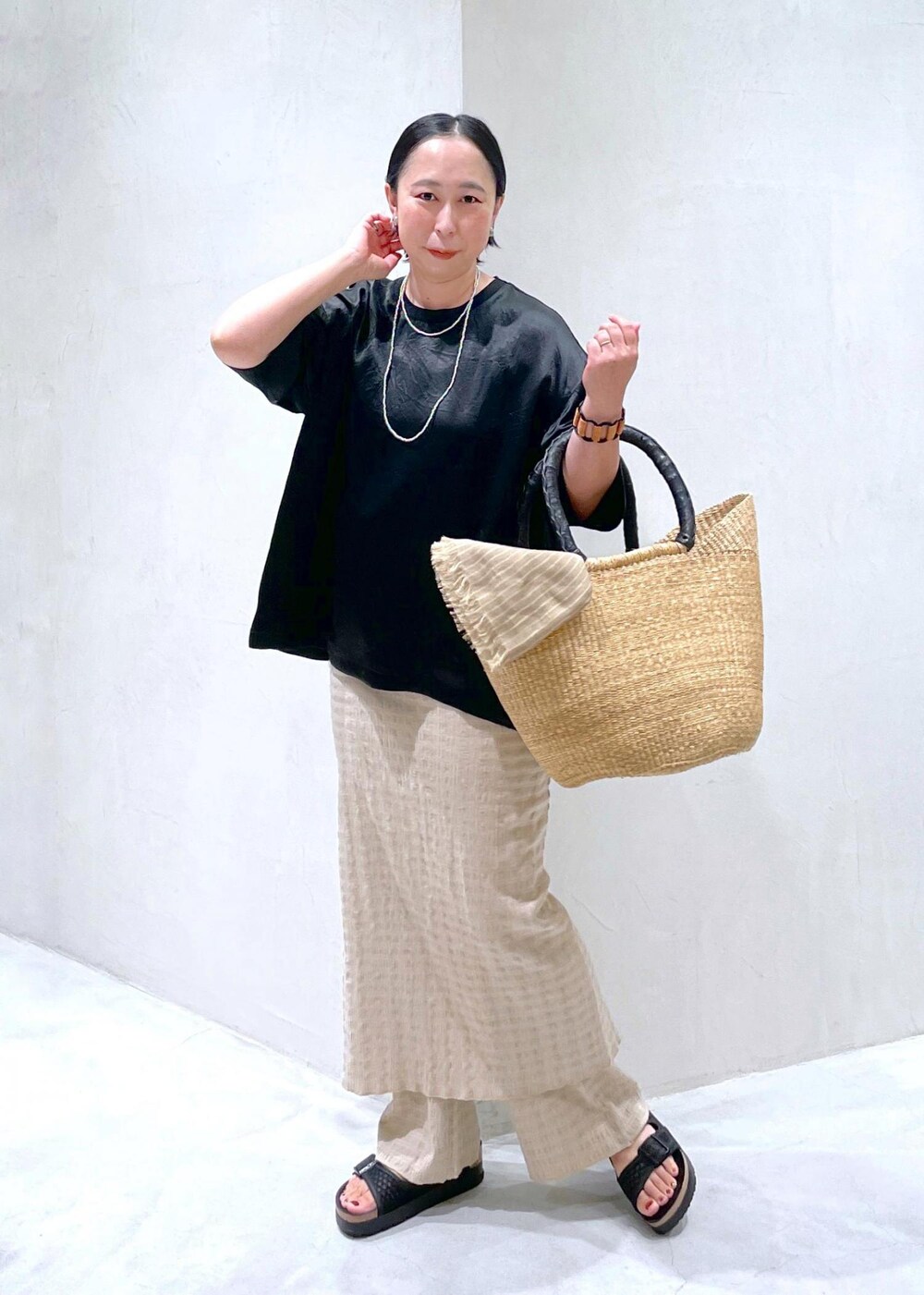 ブラック系のサンダル、ブラック系のTシャツ/カットソー、ベージュ系のかごバッグを着用したレディースの夏コーディネートの2枚目の写真