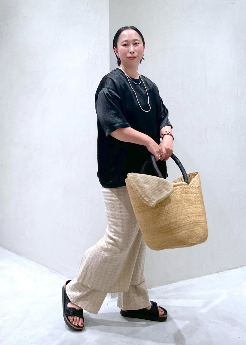 ブラック系のサンダル、ブラック系のTシャツ/カットソー、ベージュ系のかごバッグを着用したレディースの夏コーディネートの4枚目の写真