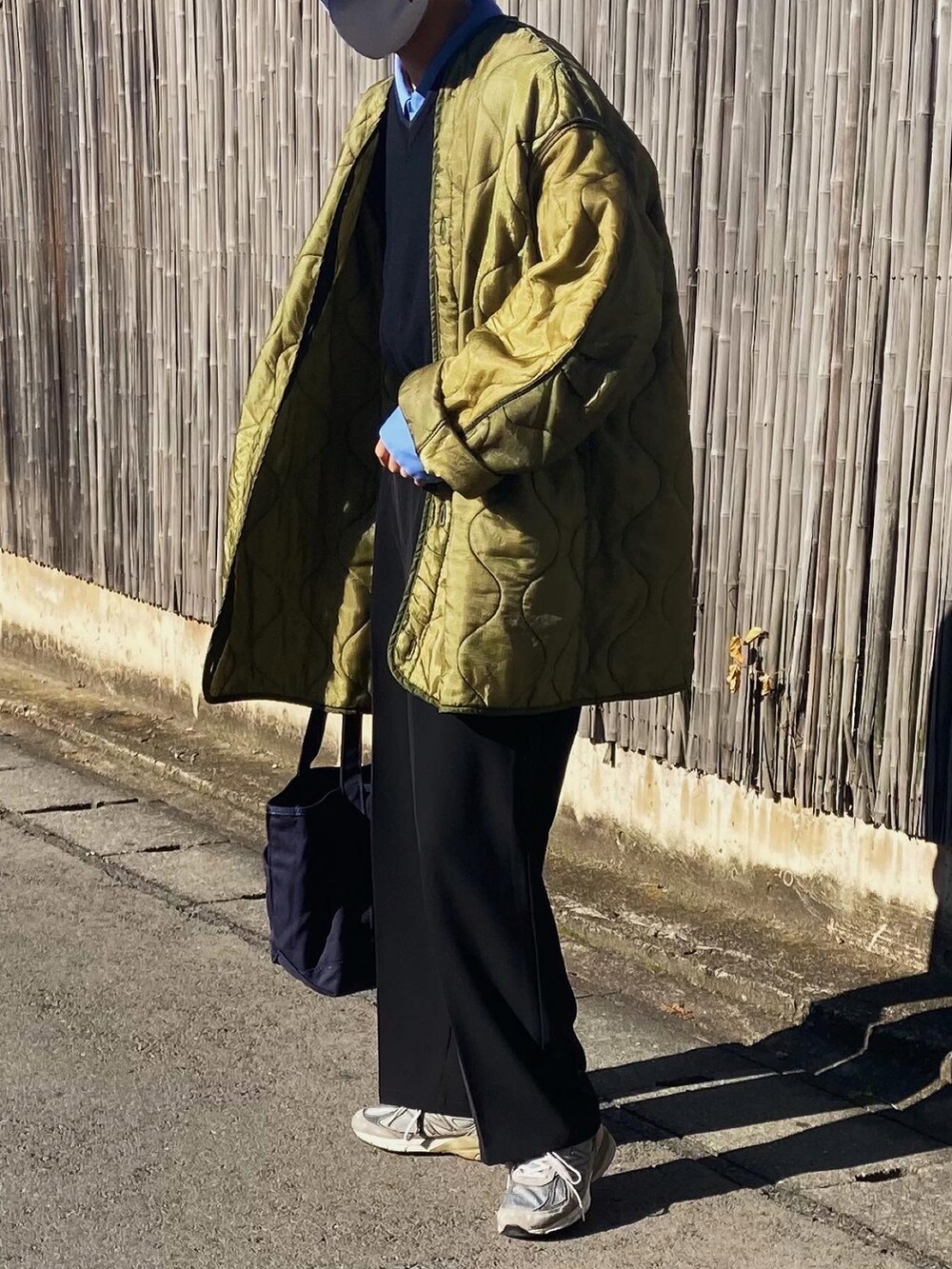 ブラック系のスラックス、グレー系のスニーカー、ブルー系のトートバッグを着用したメンズの秋コーディネートの2枚目の写真