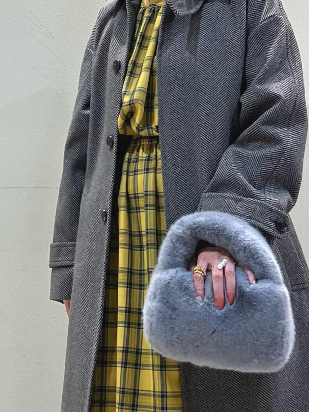 ブラウン系のステンカラーコート、グレー系のショルダーバッグ、イエロー系のワンピースを着用したレディースの冬コーディネートの2枚目の写真