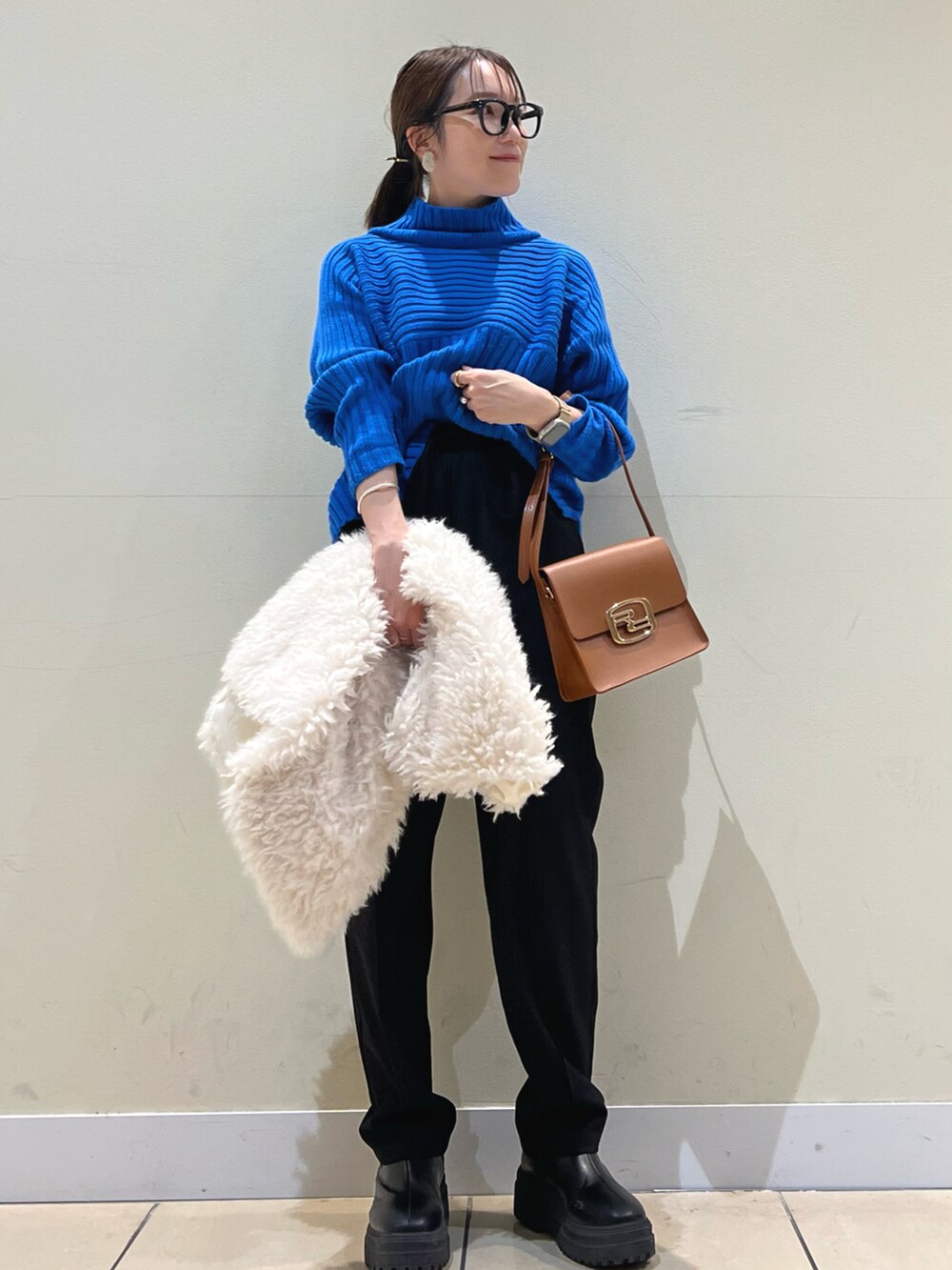 ブルー系のニット/セーター、ホワイト系のベスト、ブラック系のショルダーバッグを着用したレディースの冬コーディネートの2枚目の写真
