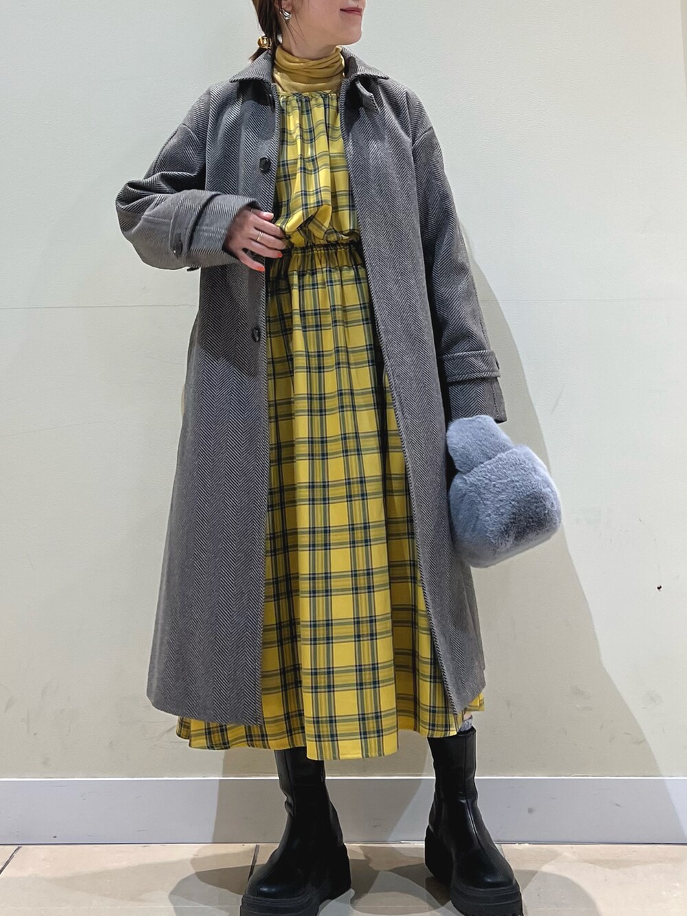 ブラウン系のステンカラーコート、グレー系のショルダーバッグ、イエロー系のワンピースを着用したレディースの冬コーディネートの4枚目の写真