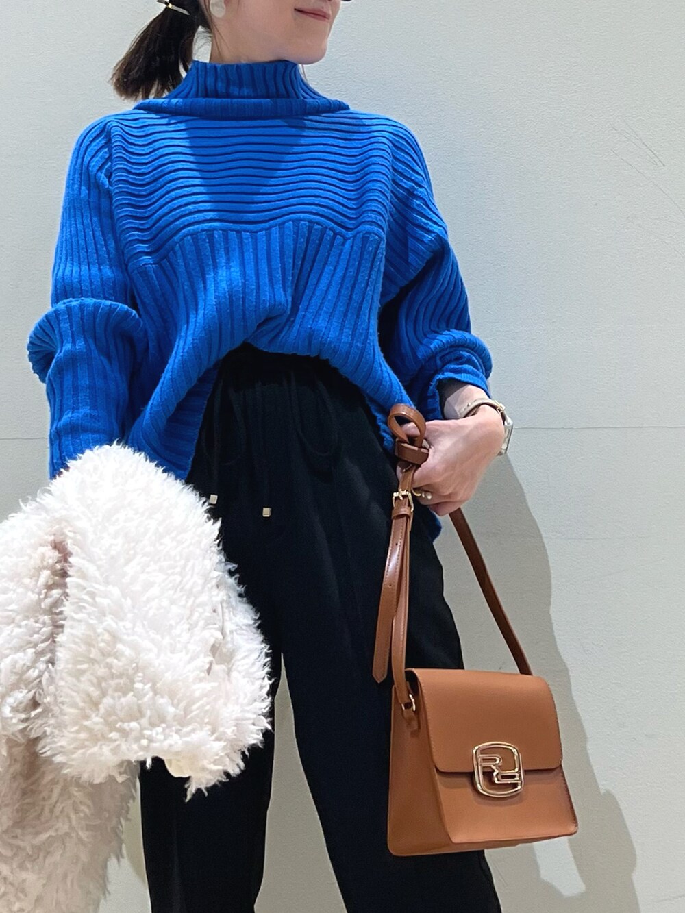 ブルー系のニット/セーター、ホワイト系のベスト、ブラック系のショルダーバッグを着用したレディースの冬コーディネートの3枚目の写真