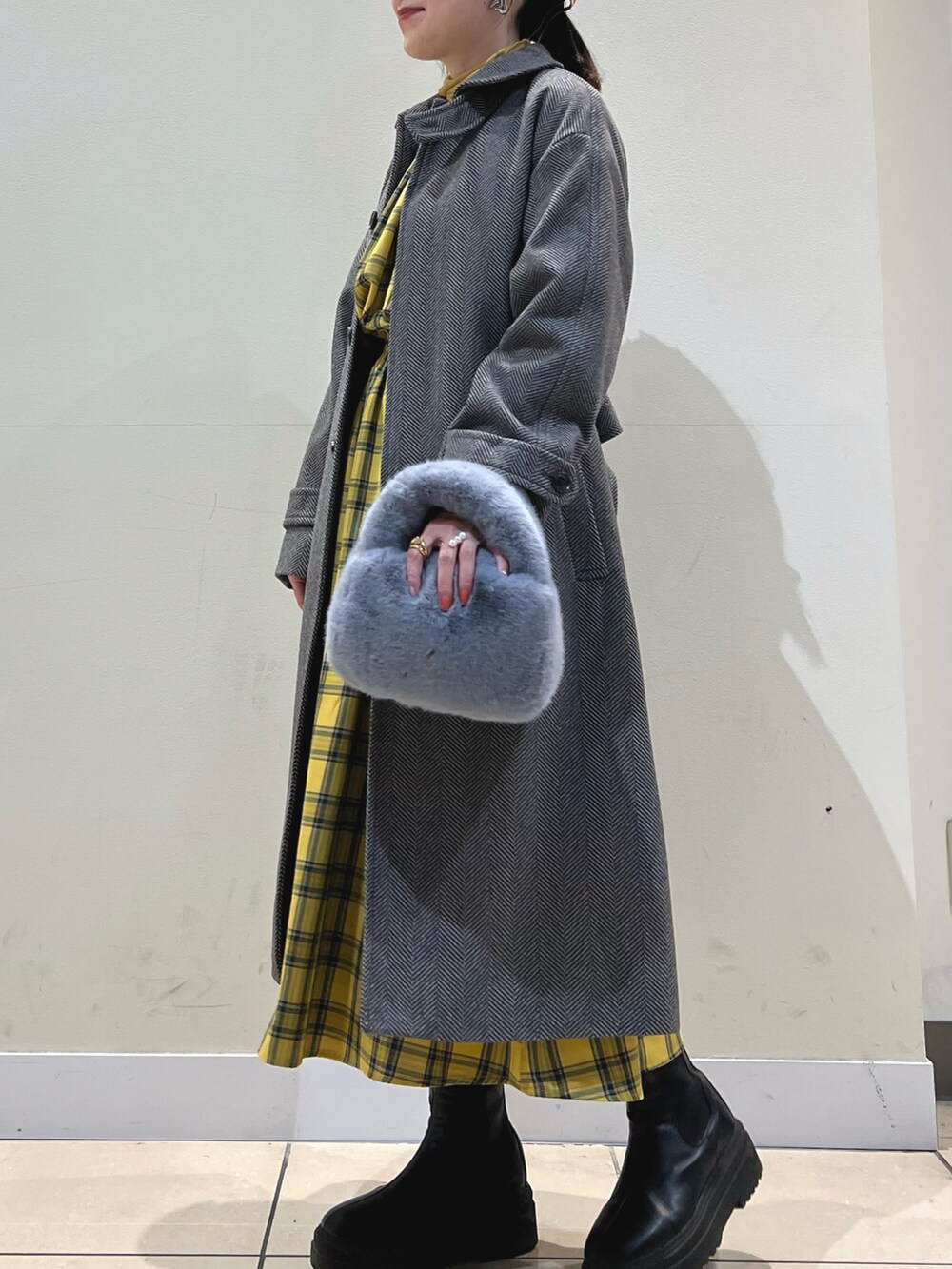 ブラウン系のステンカラーコート、グレー系のショルダーバッグ、イエロー系のワンピースを着用したレディースの冬コーディネートの3枚目の写真