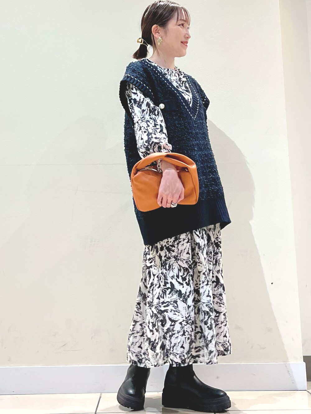 イエロー系のショルダーバッグ、ブルー系のベスト、ブラック系のワンピースを着用したレディースの秋コーディネートの2枚目の写真