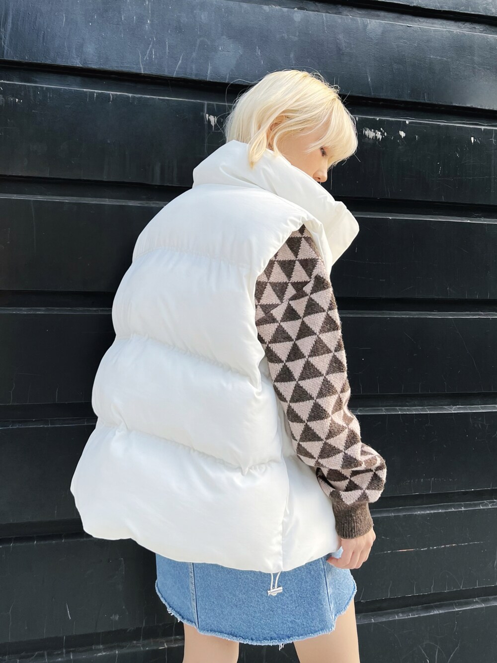 ホワイト系のダウンベスト、ブラウン系のニット/セーター、ブルー系のデニムスカートを着用したレディースの冬コーディネートの3枚目の写真