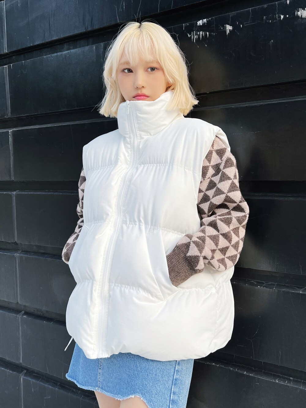 ホワイト系のダウンベスト、ブラウン系のニット/セーター、ブルー系のデニムスカートを着用したレディースの冬コーディネートの2枚目の写真