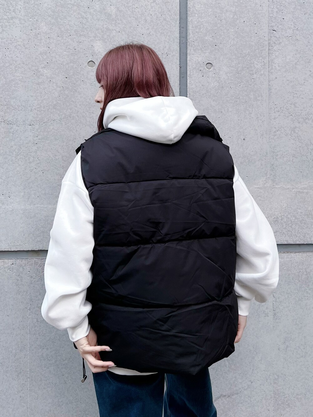 ブルー系のデニムパンツ、ブラック系のダウンベスト、ホワイト系のパーカーを着用したレディースの冬コーディネートの3枚目の写真