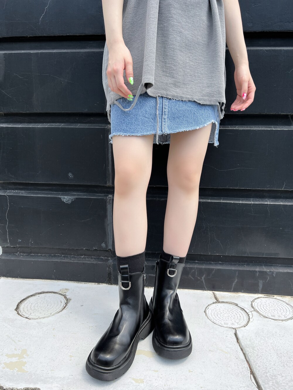 グレー系のタンクトップ、ブルー系のデニムスカート、ブラック系のブーツを着用したレディースの夏コーディネートの2枚目の写真