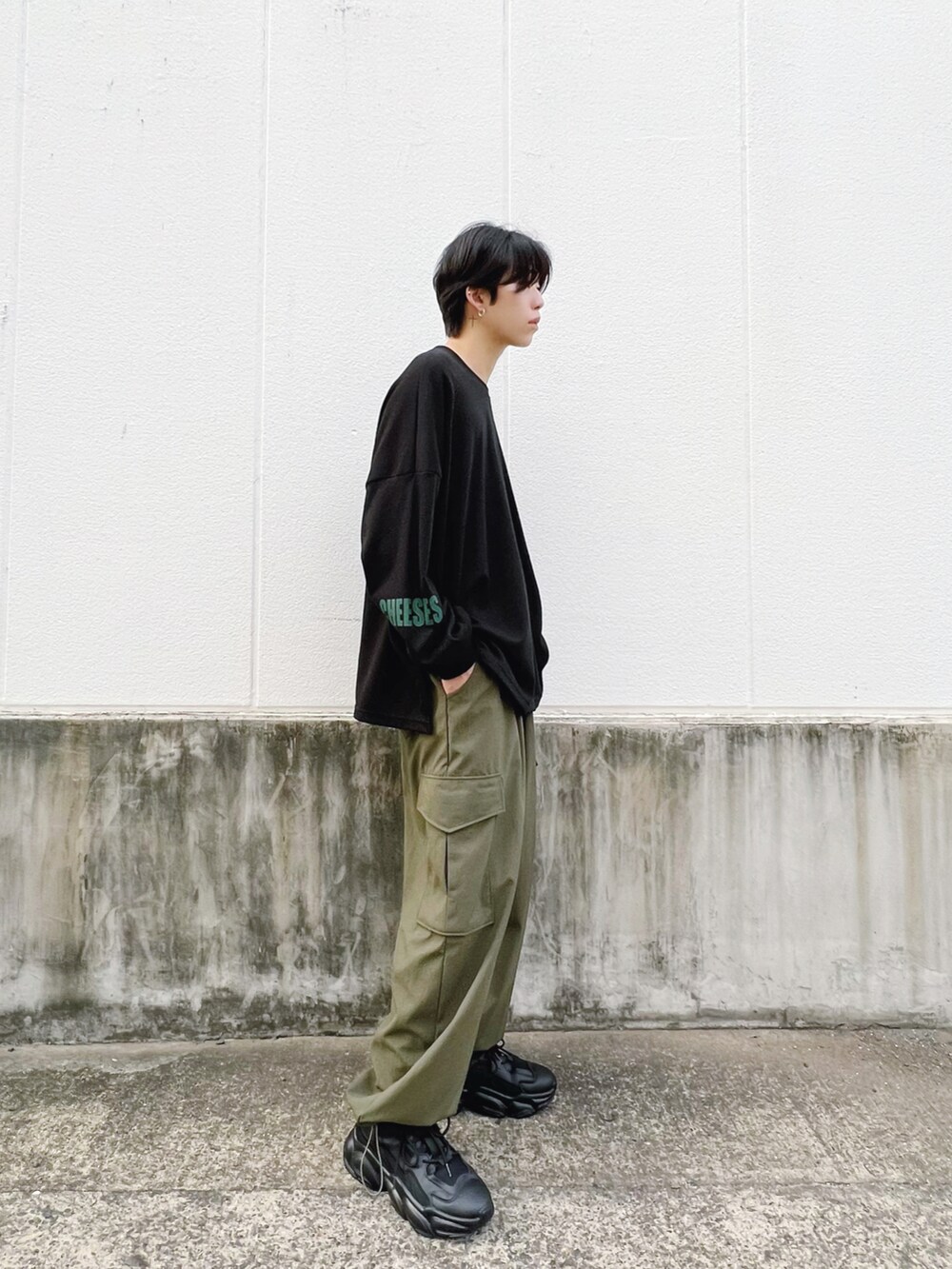 グリーン系のカーゴパンツ、ブラック系のTシャツ/カットソー、ブラック系のスニーカーを着用したメンズの秋コーディネートの2枚目の写真