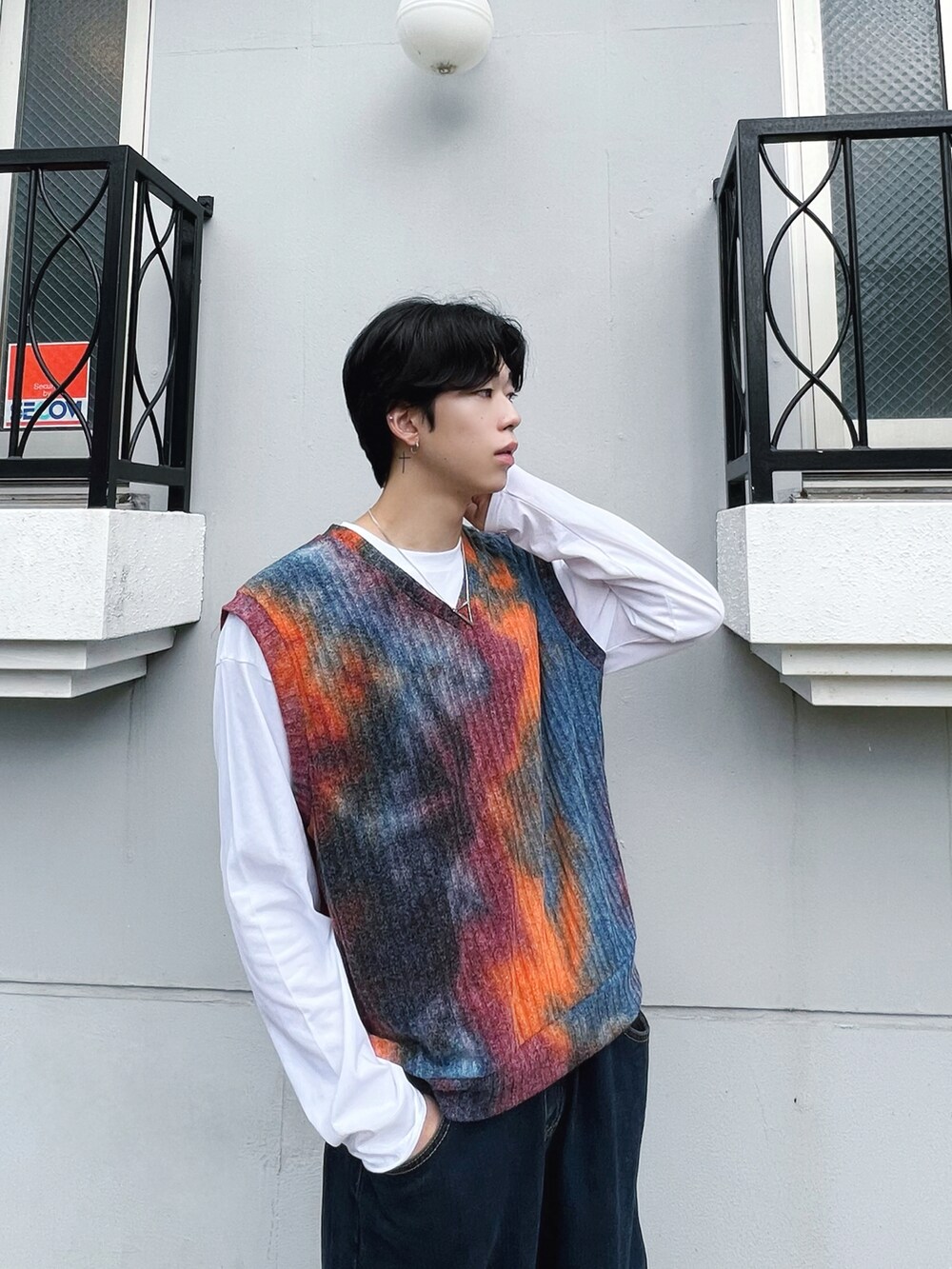 オレンジ系のベスト、ホワイト系のスニーカー、ブルー系のデニムパンツを着用したメンズの秋コーディネートの2枚目の写真