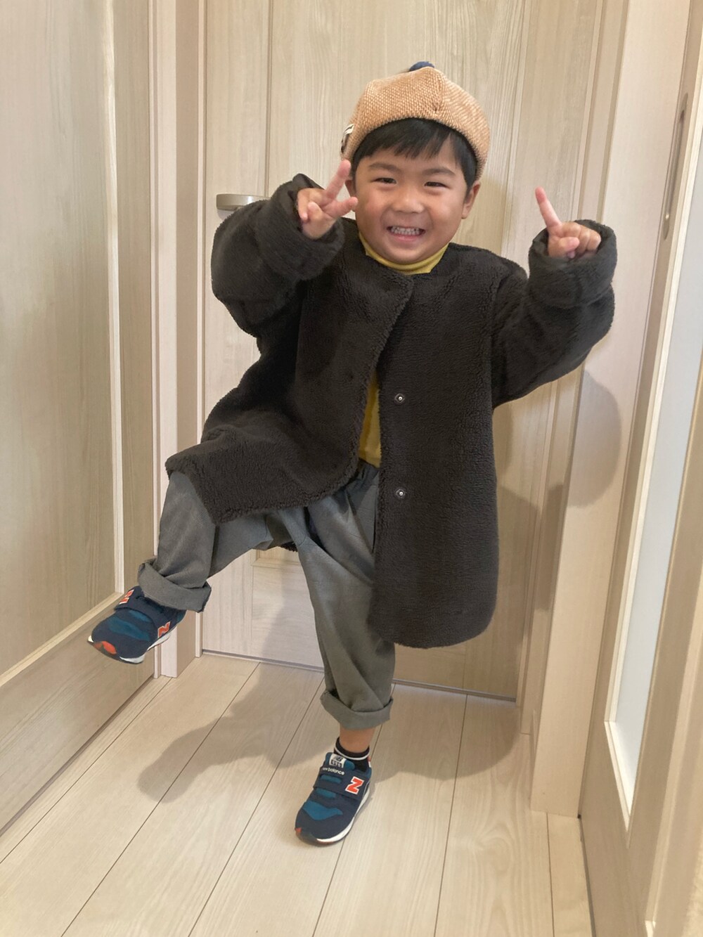 グレー系のノーカラーコート、グレー系のパンツ、ブルー系のスニーカーを着用したキッズの冬コーディネートの2枚目の写真