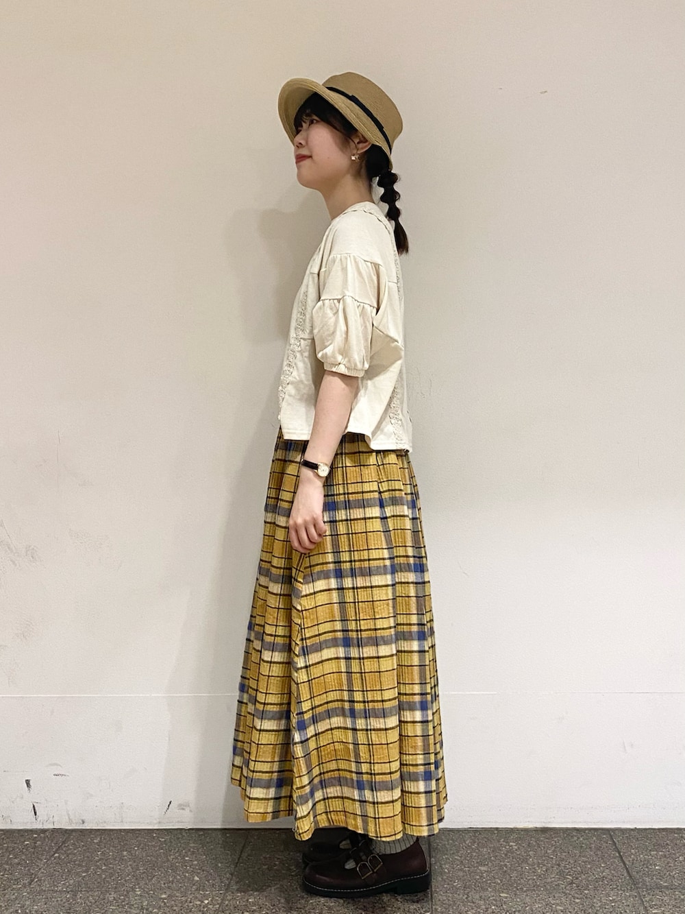 イエロー系のスカート、ホワイト系のTシャツ/カットソー、ベージュ系のハットを着用したレディースの夏コーディネートの2枚目の写真