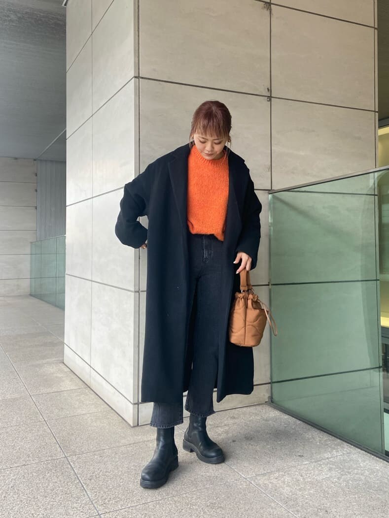 ブラック系のチェスターコート、ブラック系のデニムパンツ、オレンジ系のニット/セーターを着用したレディースの冬コーディネートの3枚目の写真