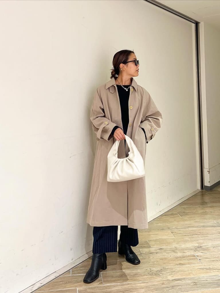 ベージュ系のステンカラーコート、ブラック系のブーツ、ブラック系のTシャツ/カットソーを着用したレディースの秋コーディネートの2枚目の写真