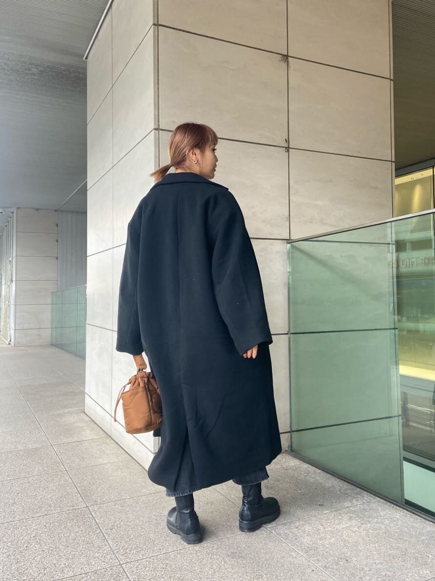 ブラック系のチェスターコート、ブラック系のデニムパンツ、オレンジ系のニット/セーターを着用したレディースの冬コーディネートの2枚目の写真