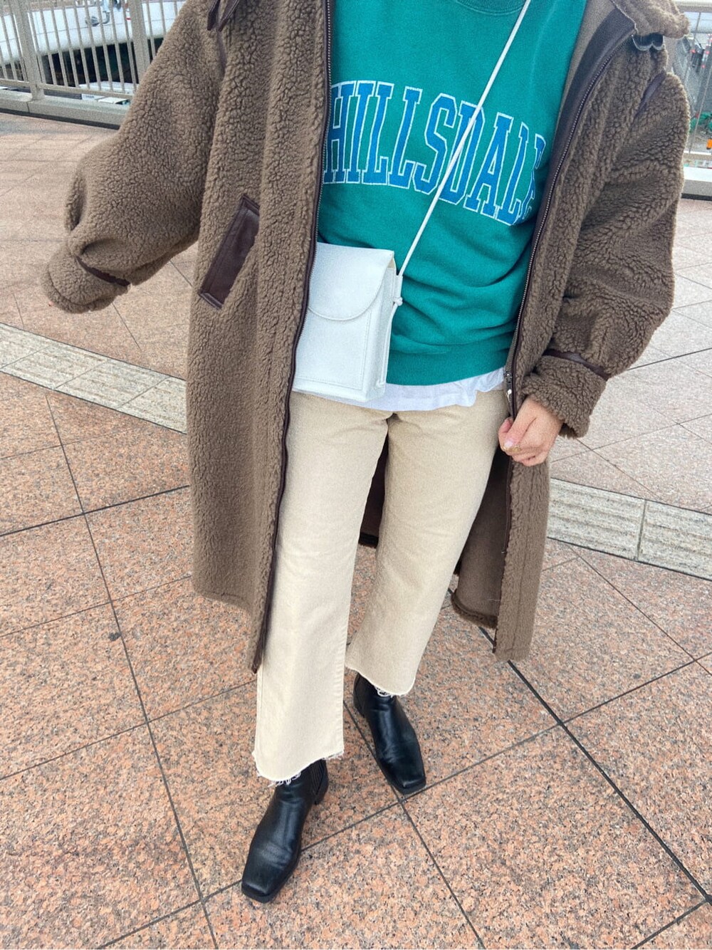 グリーン系のスウェット、ホワイト系のデニムパンツ、ホワイト系のショルダーバッグを着用したレディースの冬コーディネートの2枚目の写真