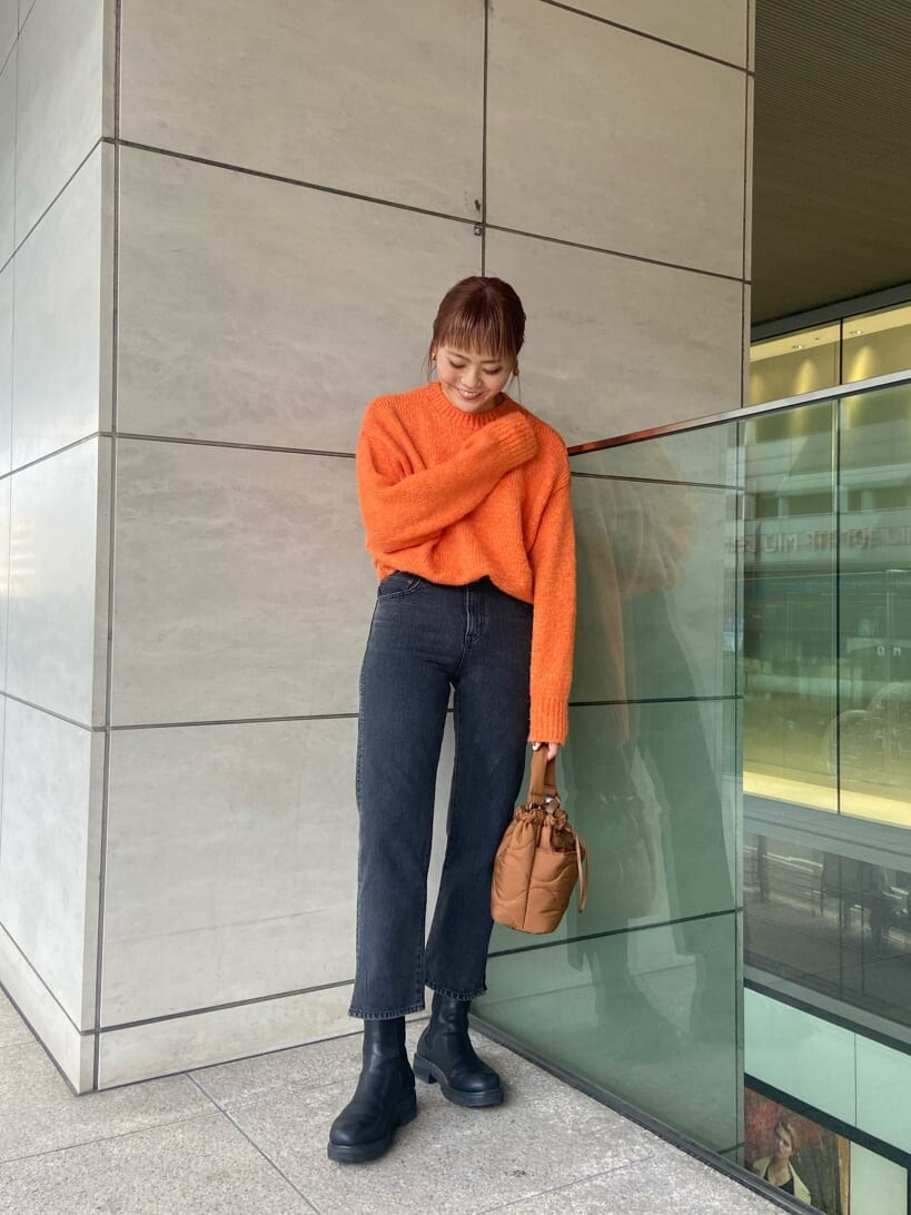 ブラック系のチェスターコート、ブラック系のデニムパンツ、オレンジ系のニット/セーターを着用したレディースの冬コーディネートの4枚目の写真
