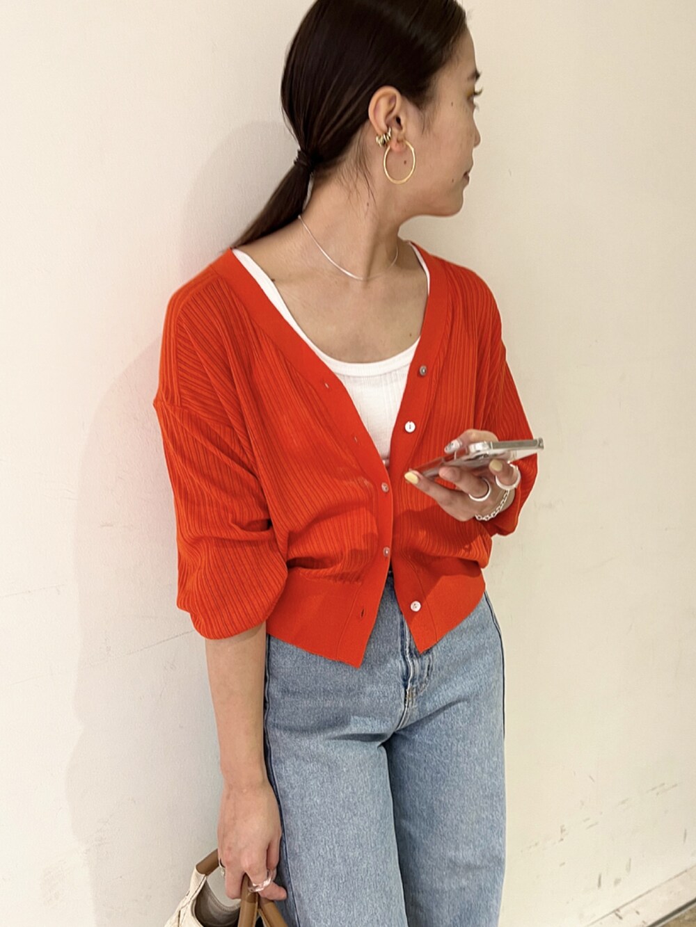 オレンジ系のカーディガン/ボレロ、ブルー系のデニムパンツ、ゴールド系のパンプスを着用したレディースの春コーディネートの2枚目の写真