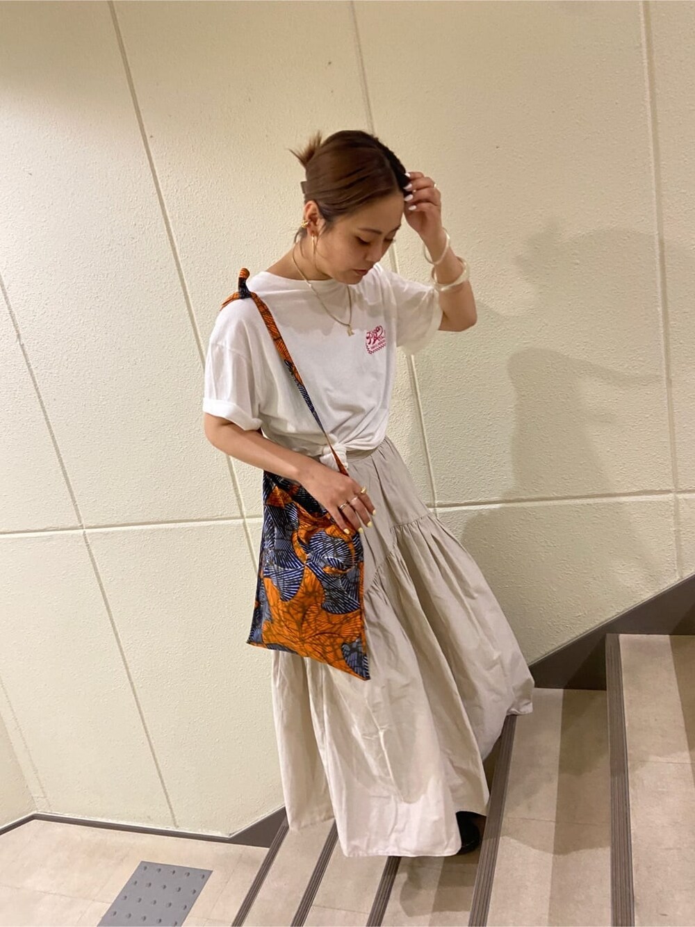 ホワイト系のスカート、オレンジ系のショルダーバッグ、ホワイト系のTシャツ/カットソーを着用したレディースの夏コーディネートの2枚目の写真